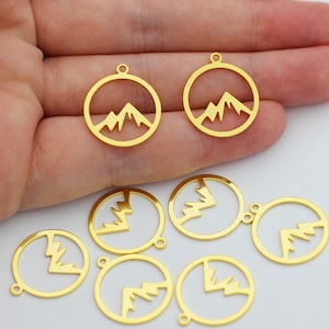 May include: Gold-coloured metal charms featuring a mountain silhouette design. The charms are round and have a hole at the top for attaching to jewellery or other crafts.