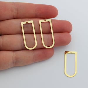 May include: Three gold-colored metal rectangular frame pendants with a small hole at the top. The pendants are slightly rounded at the top and bottom.