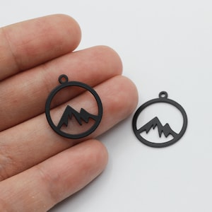 May include: Two black metal charms in the shape of a circle with a mountain silhouette inside. The charms have a hole at the top for attaching to a necklace or bracelet.