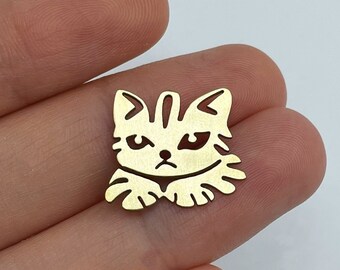 Puede incluir: Encanto de metal dorado con un diseño recortado de la cara de un gato con una expresión gruñona.
