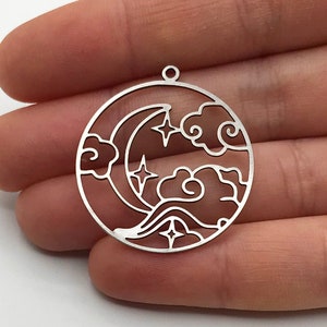 May include: Three silver metal charms in the shape of a circle with a crescent moon, stars, and clouds cut out. The charms have a hole at the top for hanging.