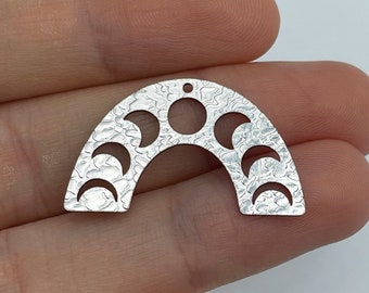 May include: A silver-colored metal arch-shaped pendant featuring a textured surface and a series of cutouts representing the phases of the moon, including crescent, half, and full moon shapes, with a small hole at the top for attachment.