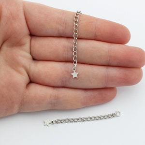 May include: Two silver-toned metal chain extenders, each featuring a small, flat, five-pointed star charm attached to one end. The chains consist of oval-shaped links and include a circular jump ring at the opposite end for secure attachment.