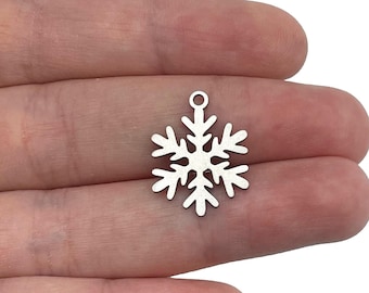 May include: A small, silver-colored metal snowflake charm featuring a symmetrical six-pointed design with intricate branching arms and a circular loop at the top for attachment, presented against a plain white background for clear visibility.