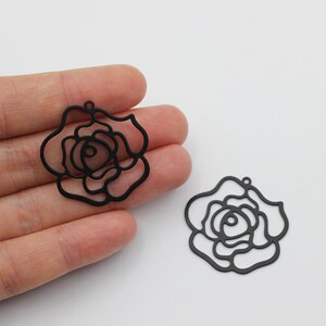 May include: Two black metal rose-shaped charms with a cutout design. The charms have a hole at the top for attaching to jewelry or other crafts.