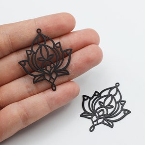 May include: Two black metal lotus flower charms with intricate cut-out designs. The charms have a hole at the top for attaching to jewelry or other crafts.