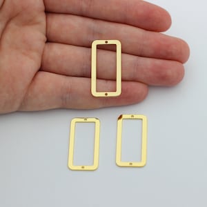 May include: Three gold-colored metal rectangular frames with rounded corners. The frames are hollow and have two small holes at the top.