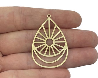 May include: A gold-toned metal pendant in a teardrop shape featuring a central circular cutout with radiating sunburst lines and two curved crescent-like arches at the bottom. The piece includes a small loop at the top for attachment.