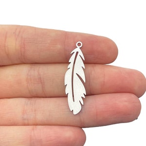 Könnte beinhalten: Silberner Federschmuck mit einer Öse oben zum Anbringen an Schmuck oder andere Bastelarbeiten.