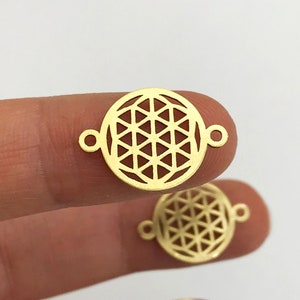 May include: Gold-toned metal charm featuring a circular geometric design with a flower of life pattern. The charm has two small loops on the sides for attaching to jewelry.