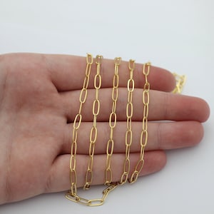 May include: A gold chain necklace with a delicate, oval-shaped link design. The chain is laid out on a hand, showcasing its length and detail.