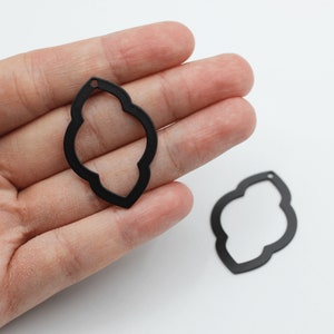 Pode incluir: Dois pingentes de metal preto com um design intrincado e vazado. Os pingentes têm a forma de um retângulo arredondado com uma borda decorativa.