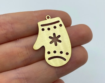 May include: A gold-toned metal charm shaped like a mitten, featuring a cutout snowflake design in the centre, horizontal rows of small circular cutouts above and below the snowflake, and a small loop at the top for attachment purposes.