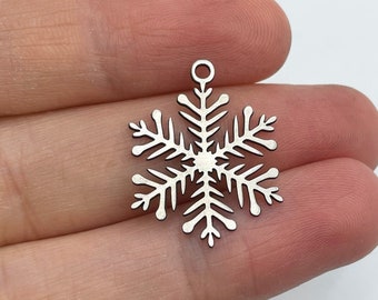 Op de afbeelding: Zilveren sneeuwvlok charme met een lus aan de bovenkant om op te hangen. De sneeuwvlok is gedetailleerd met ingewikkelde uitsnijdingen.