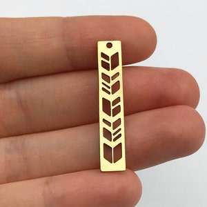 Könnte beinhalten: Goldener Metallanhänger mit geometrischem Design. Der Anhänger ist rechteckig und hat oben ein Loch zum Aufhängen.
