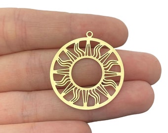 May include: A circular gold-toned metal pendant featuring a cut-out sunburst design with wavy rays radiating from a central open circle. The pendant includes a small loop at the top for attachment, showcasing a flat, metallic finish throughout.