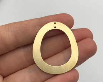 May include: A gold-toned metal pendant component with an irregular, rounded, open-center shape. The surface features a brushed finish and includes two small, vertically aligned holes at the top for attachment, suitable for jewelry making projects.