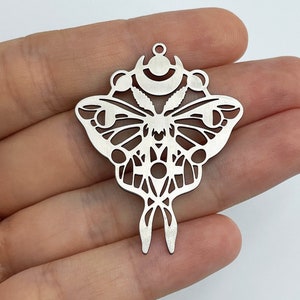 Puede incluir: Encanto de metal plateado con un diseño de corte detallado de una polilla con una luna creciente y estrellas arriba.