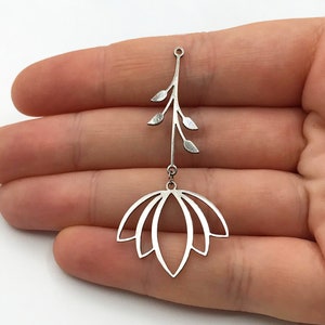 Puede incluir: Pendiente de plata con un delicado diseño de flor con tallo y hojas. El pendiente está hecho de metal y tiene un diseño recortado.