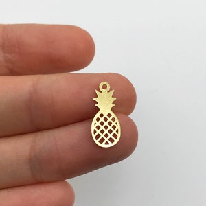 May include: Gold-colored metal pineapple charm with a cutout design. The charm is about 1 inch tall and has a loop at the top for attaching to jewelry or other crafts.
