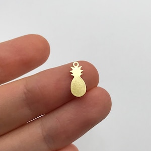 May include: A gold-coloured metal pineapple charm. The charm is approximately 2.5 cm tall and has a textured surface.