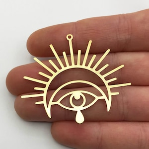 Puede incluir: Encanto de metal dorado con un ojo estilizado con una lágrima, rodeado de una luna creciente y rayos de sol.