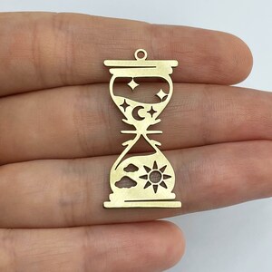 May include: Gold-toned metal hourglass charm with a sun, clouds, moon, and stars design. The hourglass is about 2 inches tall.