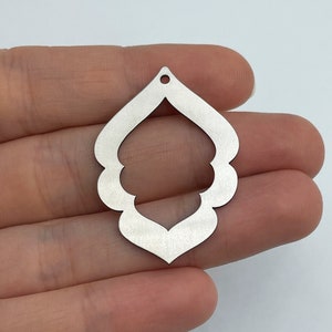 May include: A silver metal earring with a decorative, openwork design. The earring is shaped like a teardrop with a scalloped edge.