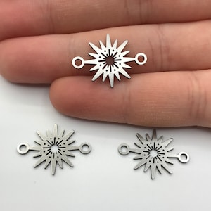 May include: Three silver metal starburst charms with two jump rings on each charm. The charms are on a white surface.
