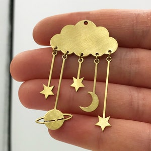 May include: Gold-toned metal charm featuring a cloud with dangling stars, a crescent moon, and a planet with rings.