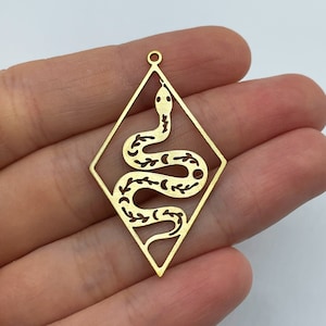 Op de afbeelding: Een goudkleurige metalen hanger in de vorm van een ruit met een uitgesneden ontwerp van een kronkelende slang. Het slangenlichaam is versierd met kleine bladpatronen en halve maanvormen. Aan de bovenkant bevindt zich een klein rond oogje.