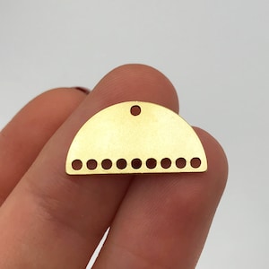 Pode incluir: Encanto de metal dourado em forma de semicírculo com um furo no topo e uma fileira de pequenos furos ao longo da borda inferior.