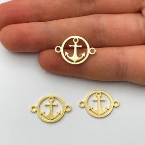 Może przedstawiać: Trzy złote metalowe zawieszki w kształcie kotwicy z okrągłym wzorem. Każda zawieszka ma dwa pierścienie do łączenia z biżuterią.