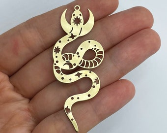 May include: A brass-colored snake pendant with a celestial design. The pendant features a snake shape with a crescent moon and star detail at the top, and star and dot cutouts along the body. It has a small loop for hanging.