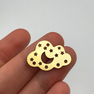 Könnte beinhalten: Goldfarbener Metallanhänger in Form einer Wolke mit einem Halbmond und ausgeschnittenen Sternen.