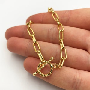 May include: A gold chain necklace with a toggle clasp. The chain is made of oval links.