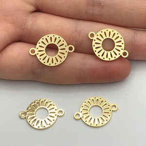 Op de afbeelding: Vier goudkleurige metalen sieradenverbinders, elk met een cirkelvormig ontwerp met een centraal gat omringd door een radiaal patroon van kleine uitsparingen en stippen, en twee kleine lusjes aan tegenovergestelde zijden van de rand.