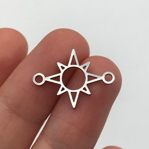 May include: Silver-toned metal charm featuring a starburst design with a circle in the center. The charm has two jump rings on either side of the starburst.