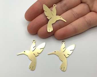 May include: Three gold-colored metal hummingbird charms. The charms are in the shape of a hummingbird in flight. The charms have a hole at the top for attaching to a necklace or bracelet.