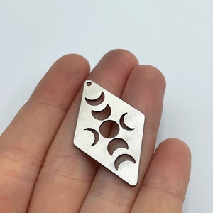 May include: A silver diamond-shaped charm with a cutout design of the moon phases. The charm has a hole at the top for attaching to a necklace or bracelet.