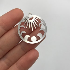 May include: Silver metal charm with a sun and moon design. The sun is in the center with rays extending out. The moon is in a crescent shape around the sun.