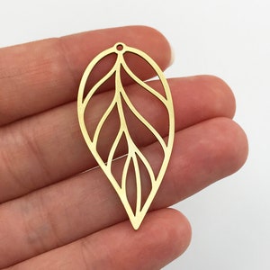 Op de afbeelding: Gouden bladhanger met een delicaat, ingewikkeld ontwerp. Het blad is uitgesneden, waardoor een kant-effect ontstaat. Het heeft een klein gaatje bovenaan om op te hangen.