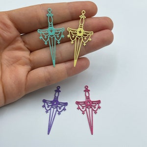 May include: Four metal sword charms with a star design. The charms are in four different colors: teal, yellow, purple, and pink.
