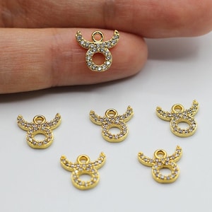 May include: Six gold-tone Taurus zodiac charms with clear crystal accents. The charms are small and delicate, perfect for adding a touch of sparkle to jewelry.