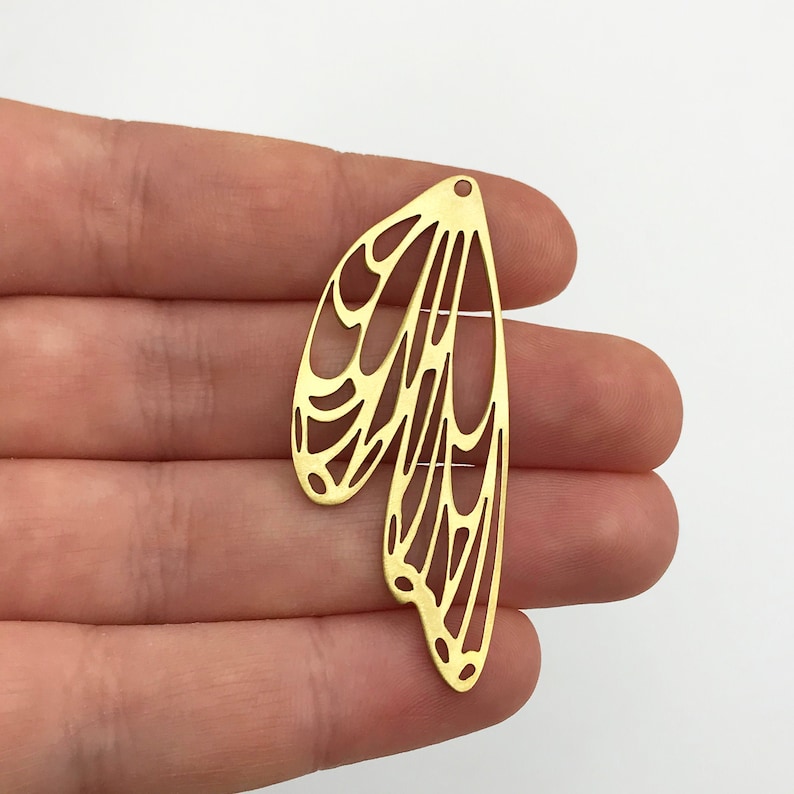 Pu&ograve; includere: Taglio in metallo dorato di un paio di ali di farfalla con un design delicato e intricato.