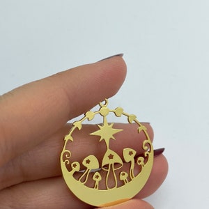 May include: Gold-toned metal pendant featuring a circular design with a star and mushrooms. The pendant is cut out and has a detailed design.