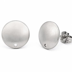 May include: A pair of silver-toned circular stud earrings with a brushed metal finish. Each earring features a flat, round disc design with a small circular hole positioned near the bottom edge and a standard post backing for secure attachment.