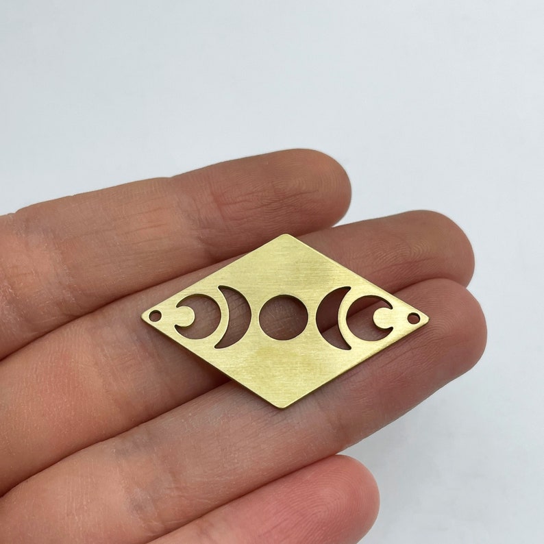 Peut inclure: Un charme en m&eacute;tal dor&eacute; en forme de diamant avec trois d&eacute;coupes en forme de croissant de lune. Le charme a une finition bross&eacute;e.