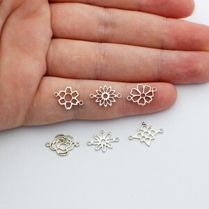 Puede incluir: Seis dijes conectores de metal plateado con varios dise&ntilde;os florales. Los dijes son calados, con formas que incluyen una flor, una margarita y una estrella. Los dijes se muestran sobre una superficie blanca.