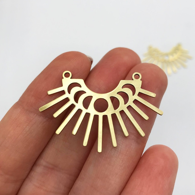May include: A pair of gold-toned metal earring blanks with a sunburst design. The blanks have a hole at the top for attaching earring wires.